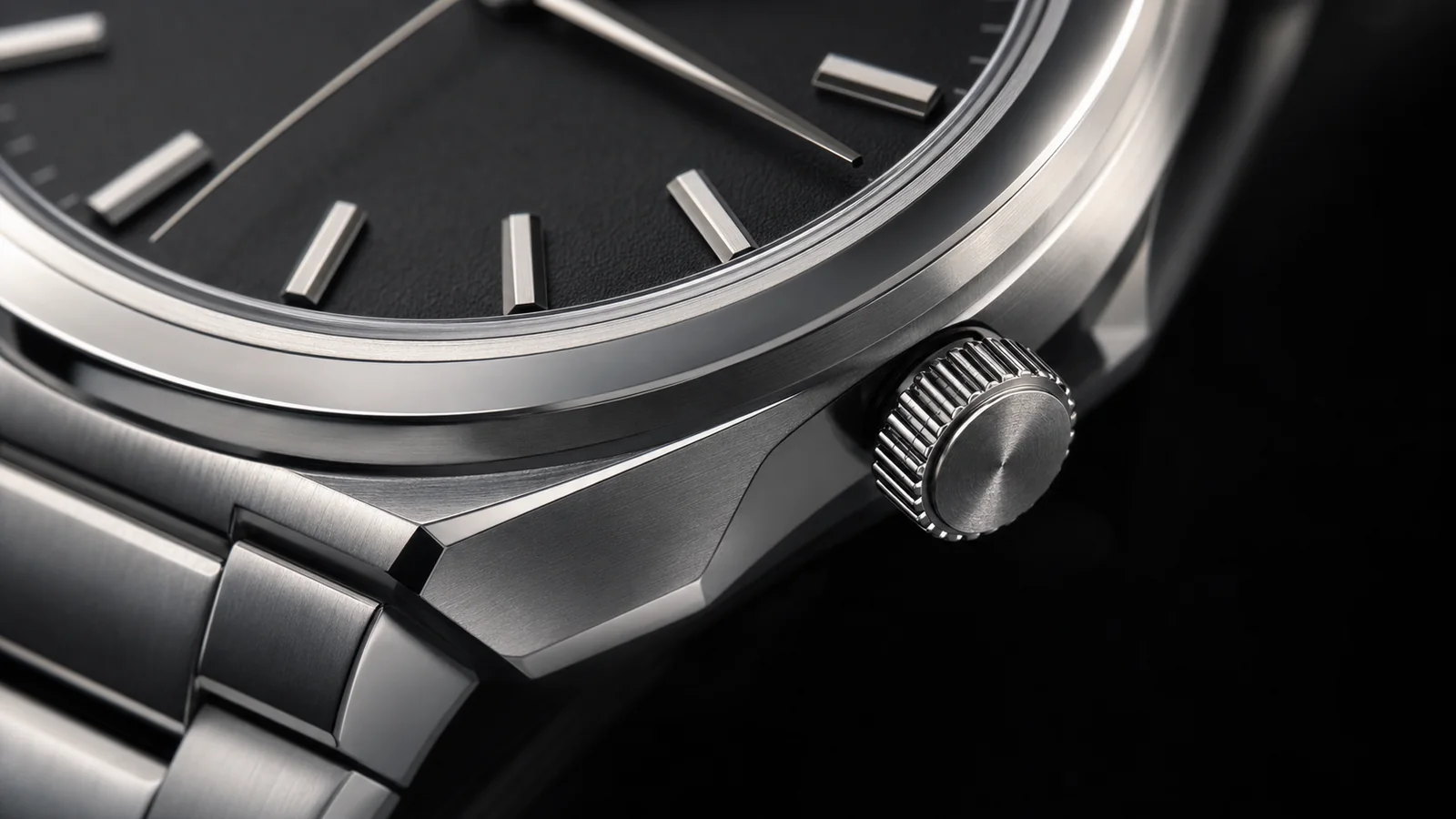 Macro detail of an unbranded brushed-steel watch case, crown, dial and bracelet.